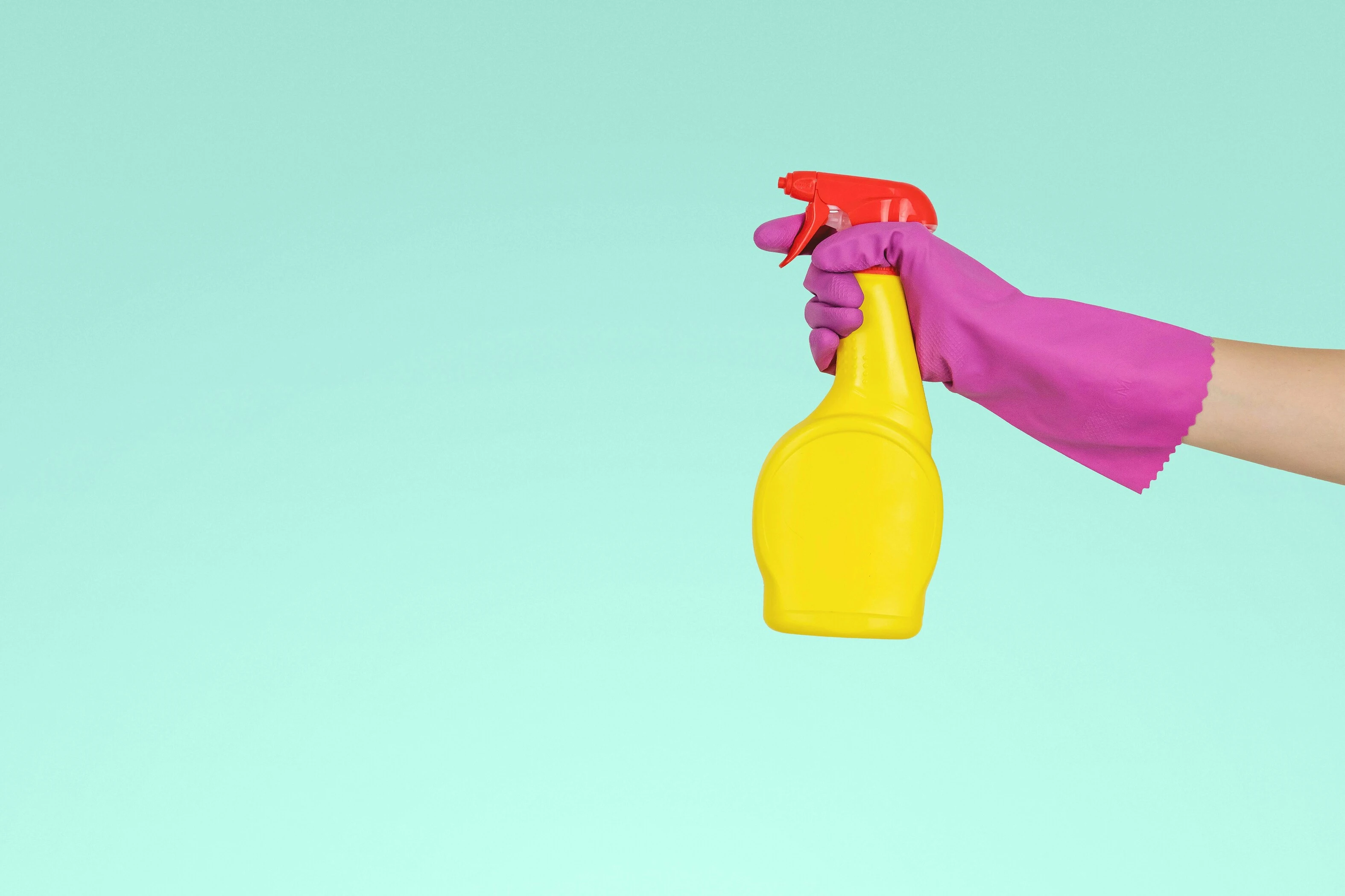 A hand in a dishwashing glove is holding a sprayer to clean a surface